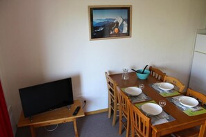 A dining area with a wooden table set for four, a television on a stand, and a framed picture on the wall. - 200m from resort center, 2nd floor, view mountain, balcony, tv, ski locker, 32m², Superdévoluy (Le Dévoluy)