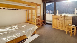 Ein Zimmer mit einem Etagenbett, einem kleinen Schreibtisch mit Stuhl und einem Fenster mit Blick auf Gebäude und Berge.