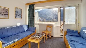 Ein gemütliches Zimmer mit einem blauen Sofa, einem Holztisch und Bergblick durch ein Fenster.