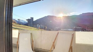 Ein Balkon mit zwei weißen Stühlen und Blick auf eine Stadtlandschaft mit Bergen im Hintergrund.