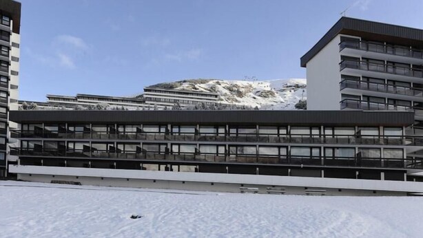 Ein modernes Gebäude mit mehreren Stockwerken und großen Fenstern, vor einer verschneiten Landschaft mit einem Berg im Hintergrund.