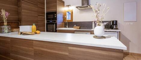 A modern kitchen with a large island, built-in oven, and a stainless steel range hood.