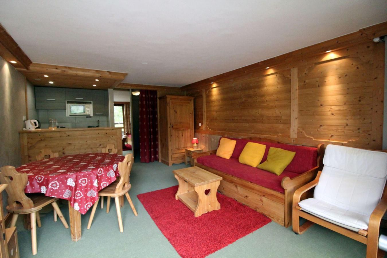 A cozy room with a wooden dining table, a red sofa with cushions, a wooden chair, and a small wooden stool.