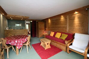 A cozy room with a wooden dining table, a red sofa with cushions, a wooden chair, and a small wooden stool.