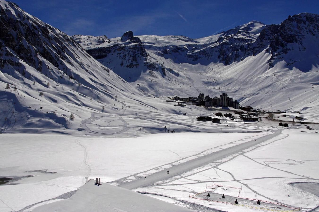 Een besneeuwd berglandschap met een skigebied, inclusief skipistes en een klein dorp met gebouwen.