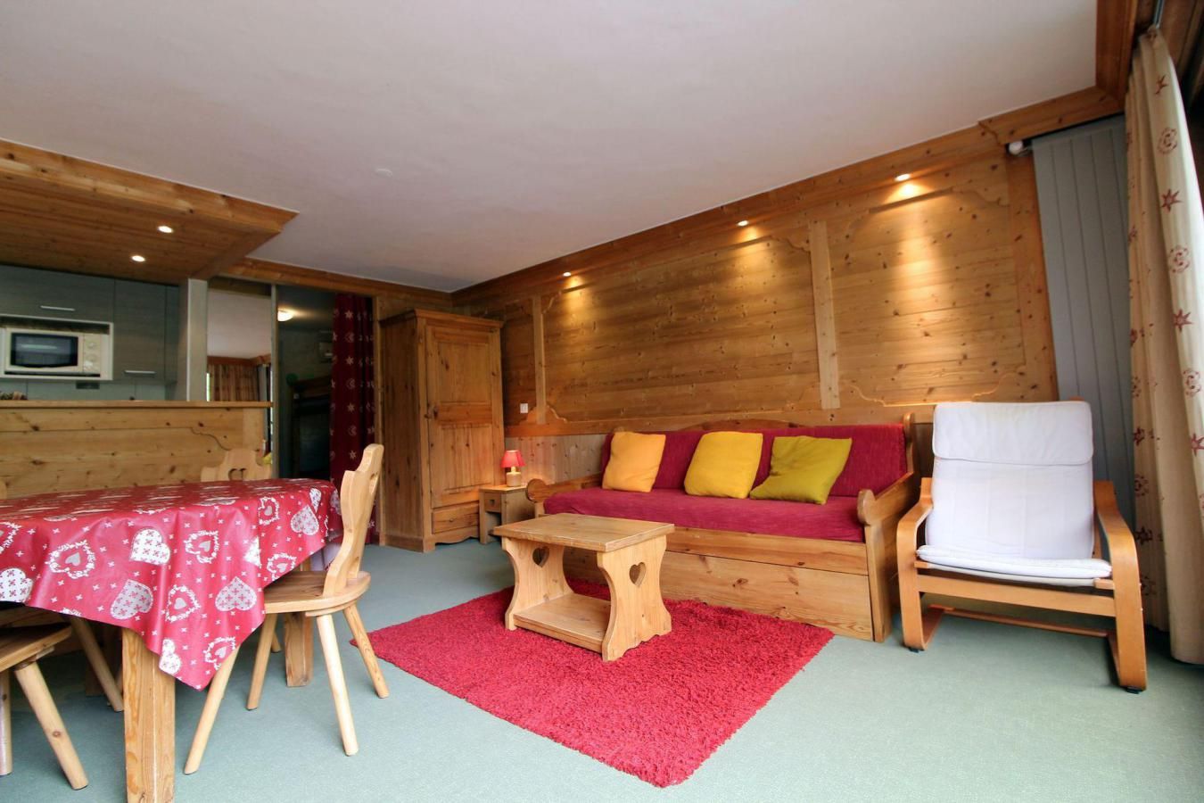 A cozy room with a wooden interior, a red sofa with cushions, a white chair, a wooden table, and a red rug.
