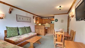 A cozy living room with a sofa, a wooden dining table, and chairs. A kitchen with wooden cabinets and a microwave is visible in the background. - 10m from ski slopes, 6th floor, balcony, 40m², Méribel-Mottaret (Méribel - Les Allues)