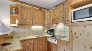 A kitchen with wooden cabinets, a sink, a stove, and a microwave. - 10m from ski slopes, 6th floor, balcony, 40m², Méribel-Mottaret (Méribel - Les Allues)