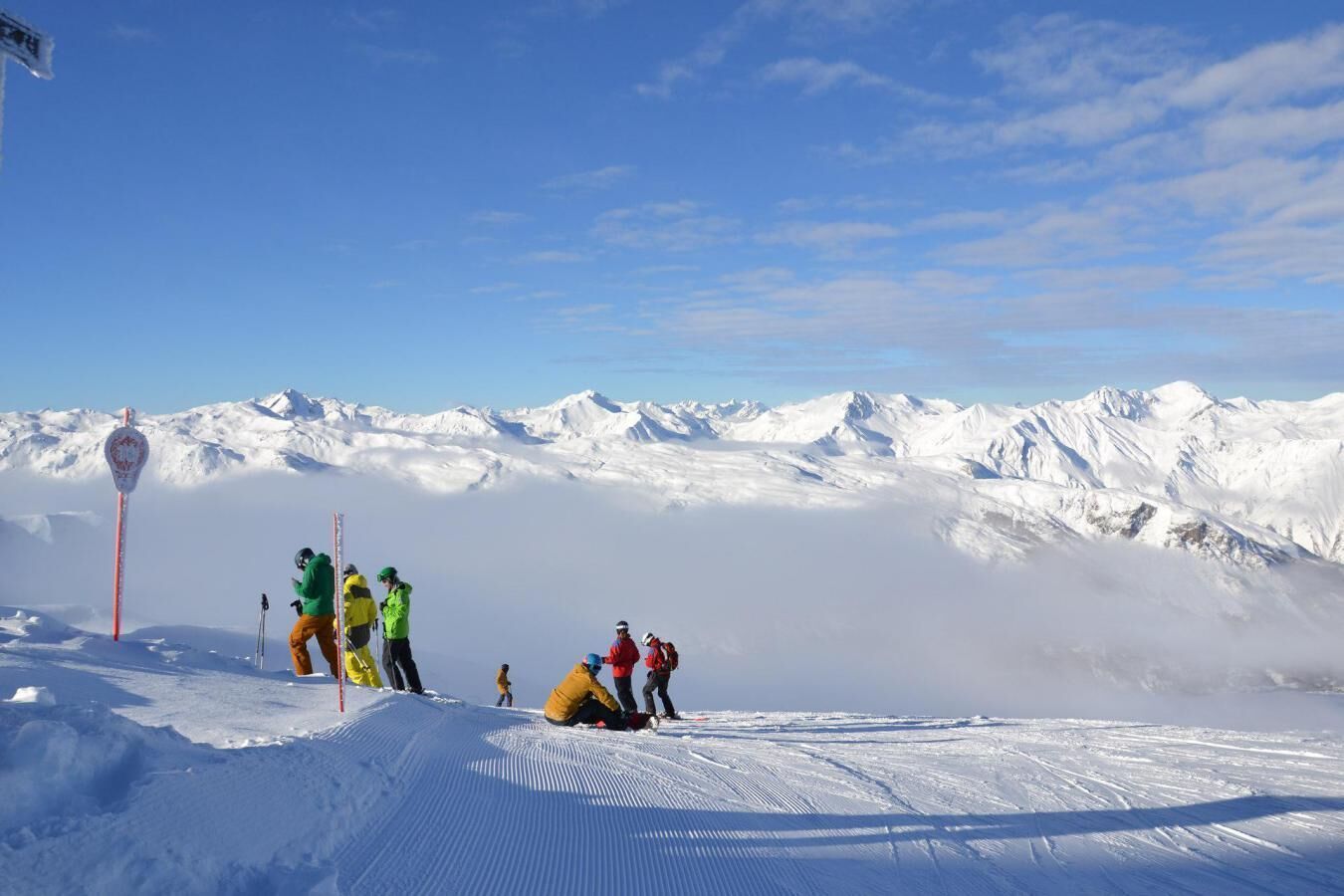 Eine verschneite Berglandschaft mit Skifahrern und einem Wegweiser.