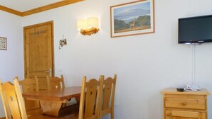 A dining area with a wooden table and chairs, a wall-mounted TV, and a small cabinet with a phone and a remote control. - 10m from ski slopes, 6th floor, balcony, 40m², Méribel-Mottaret (Méribel - Les Allues)