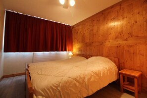 A room with a bed, a nightstand, a window with curtains, and wooden paneling on the walls.