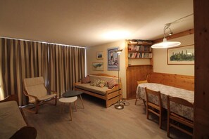 A cozy living room with a sofa, a chair, a dining table, and a bookshelf.