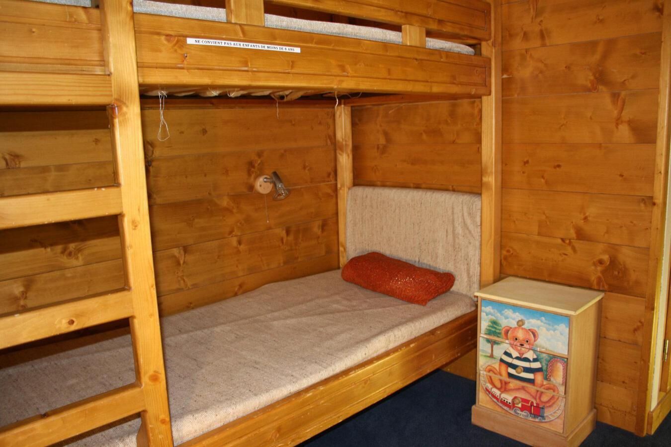 Un lit superposé en bois avec un oreiller rouge et une boîte à jouets.