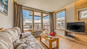 A cozy living room with a sofa, a coffee table with breakfast items, a TV, and large windows with a mountain view.
