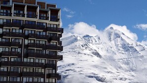 A multi-story hotel with balconies, set against a backdrop of a snow-covered mountain.
