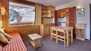 A cozy room with a wooden interior, a large window with a view of a snowy mountain, a wooden table with chairs, and a small wooden bench. - 10m from ski slopes, 2nd floor, balcony, 33m², Méribel-Mottaret (Méribel - Les Allues)