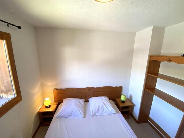 A single bed with a wooden headboard in a room with white walls and a window.