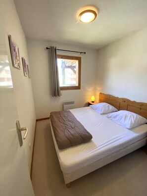 A single bed with a wooden headboard, a bedside lamp, and a window with curtains.