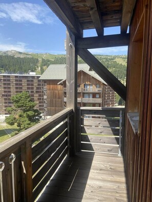 A wooden balcony with a view of a building with multiple balconies and a mountainous landscape in the background.