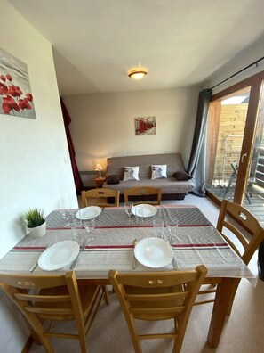 A dining area with a table set for four, a sofa in the background, and a balcony with a view.