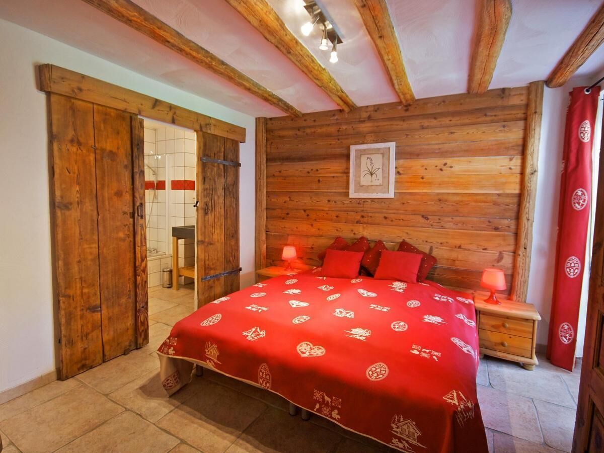 A bedroom with a wooden headboard, a red bedspread with white patterns, and a wooden floor.