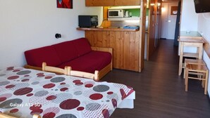 Una habitación acogedora con un sofá rojo, un cabecero de madera, una kitchenette con microondas y un televisor montado en la pared.