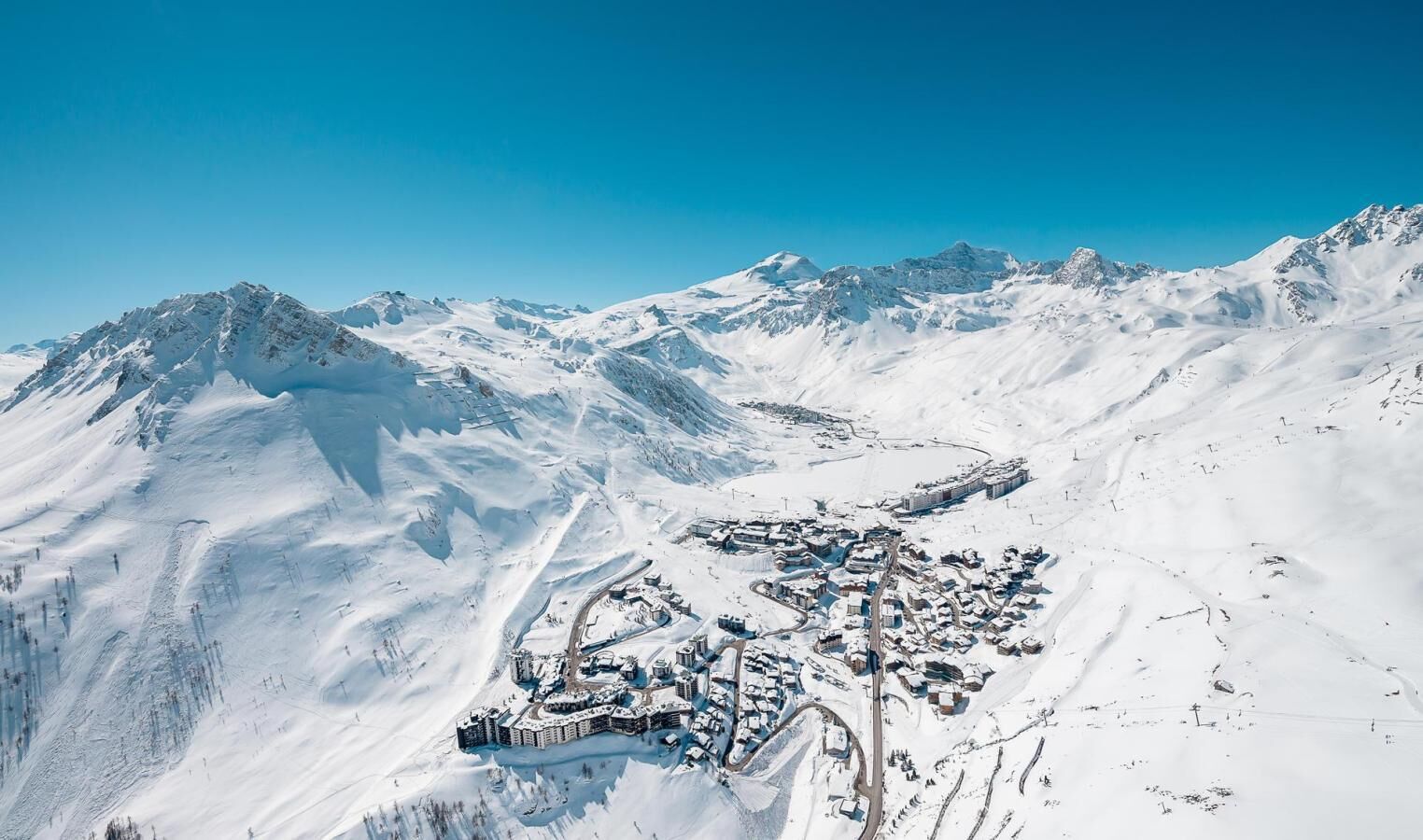 Schneebedeckte Berglandschaft mit einer Stadtansicht, die sich durch eine zentrale Ansammlung von Gebäuden, Straßen und ein kleines Gewässer auszeichnet.