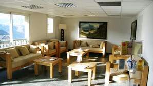Una habitación amplia con muebles de madera, ventanas grandes y un cuadro en la pared.