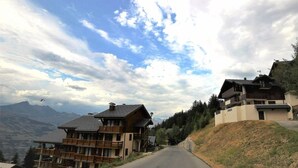 A mountain road with wooden buildings on either side, featuring balconies and a view of the mountains in the background. - 150m from ski slopes, 1st floor, terrace, tv, 75m², Peisey-Vallandry (Landry)