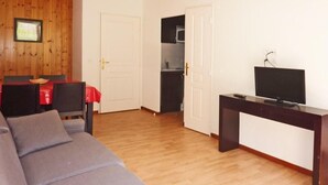 Ein Wohnzimmer mit grauem Sofa, einem Fernsehgerät auf einem Schrank und einem durchgehenden offenen Durchgang zum Küchenbereich.