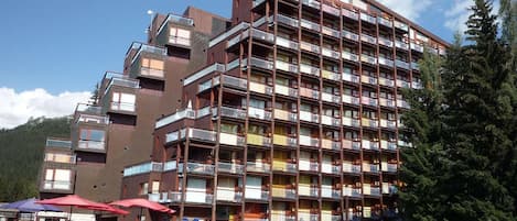A multi-story hotel with balconies, outdoor seating, and a mountainous backdrop.