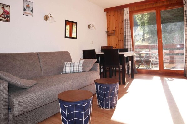 Un salon confortable avec un canapé, deux petites tables d’appoint, une petite table avec des chaises et une vue à travers une porte vitrée.