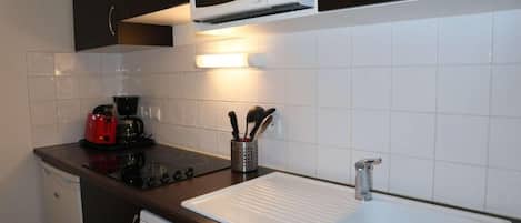 A compact kitchen with a microwave, stove, coffee maker, and a sink.