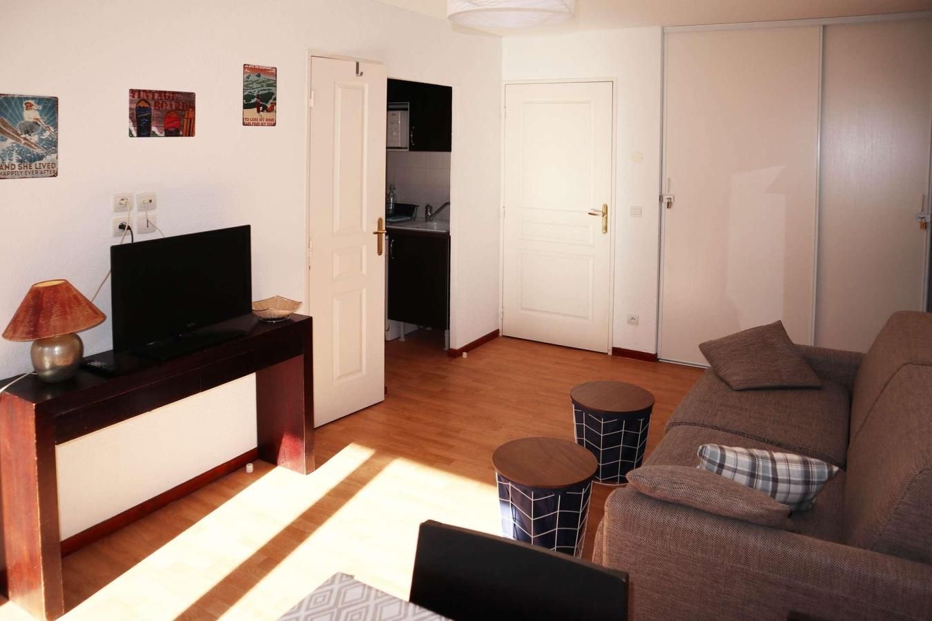 Een woonkamer met een bank, een televisie, een lamp en een keuken op de achtergrond.