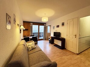 A cozy living room with a sofa, a television, and a dining area with a table and chairs.