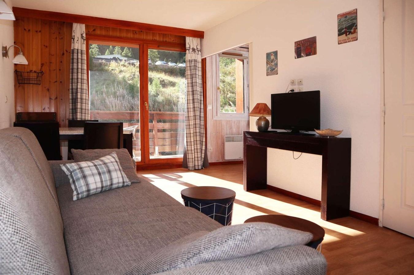 A cozy living room with a sofa, a television on a stand, and a view of a forested area through large windows.