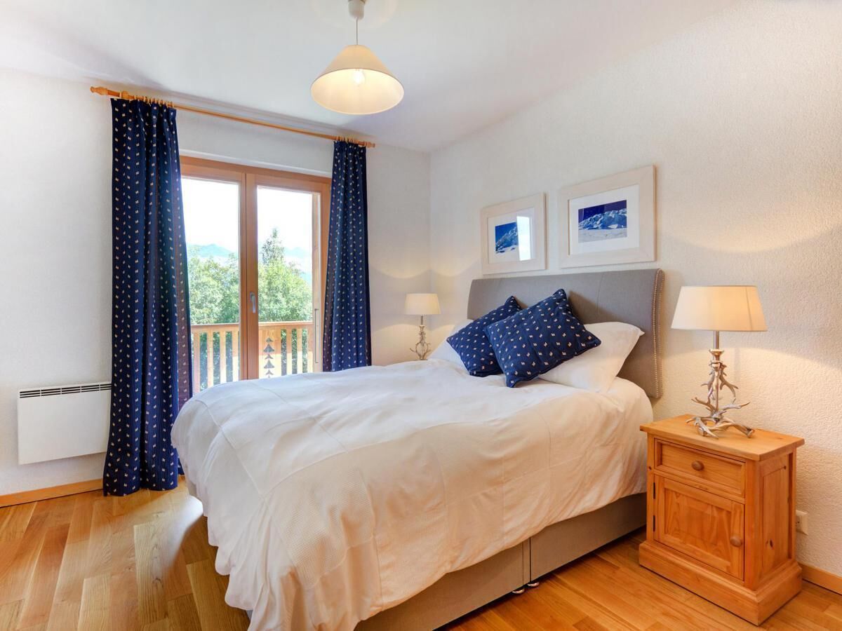 A bedroom with a large bed, a wooden nightstand, two bedside lamps, and a window with curtains.