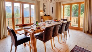 A dining area with a wooden table and chairs, a chandelier, and large windows with a view of mountains.