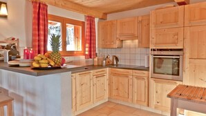 A kitchen with wooden cabinets, a central island with fruit, a stove, and a window with curtains.