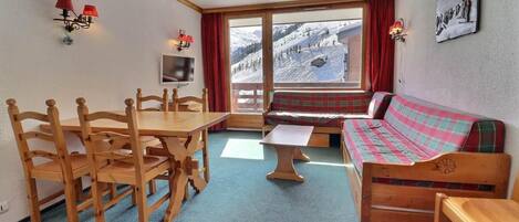 A cozy room with a wooden dining table, a sofa, and a view of a snowy mountain.