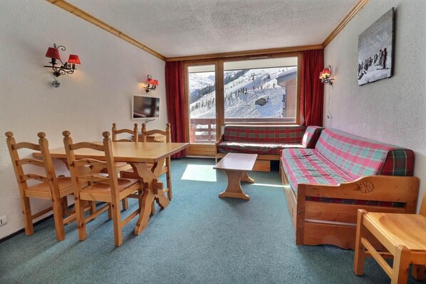 A cozy room with a wooden dining table, a sofa, and a view of a snowy mountain.