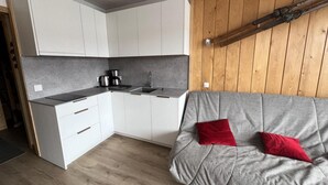 Eine kleine Küche mit weißen Schränken, einer grauen Arbeitsplatte und einer Holzwand.