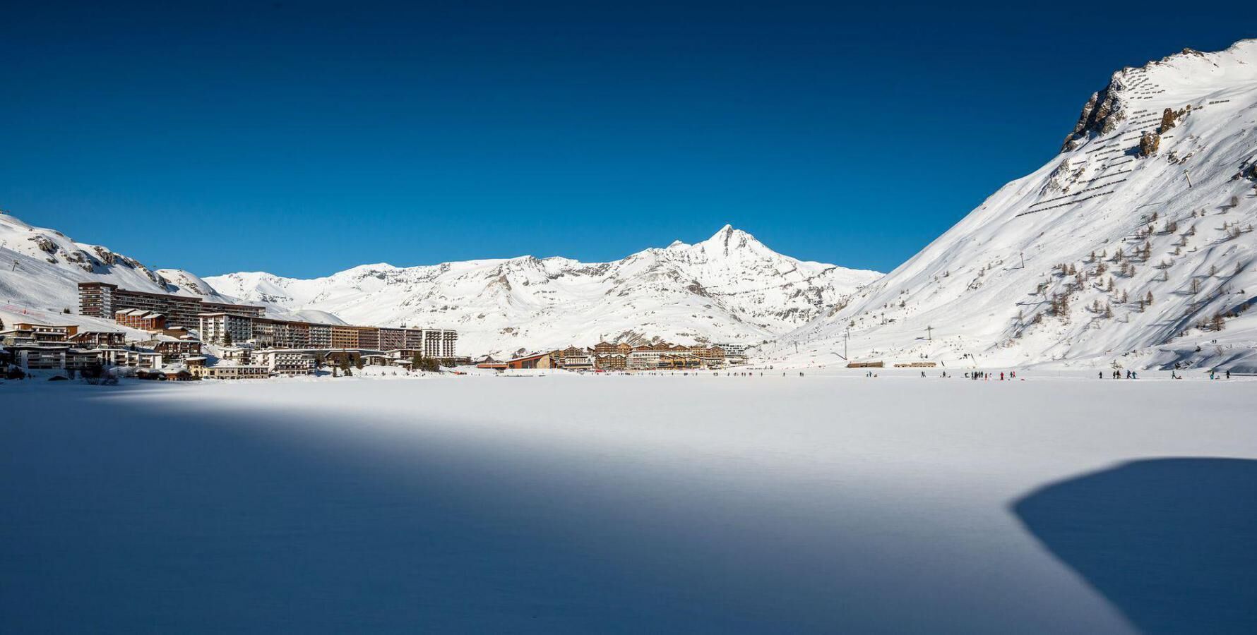 A snow-covered mountain resort with buildings and a clear blue sky.