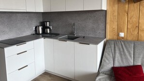 Eine kleine Küche mit weißen Schränken, einer grauen Arbeitsplatte, einer Kaffeemaschine und einem Spülbecken.