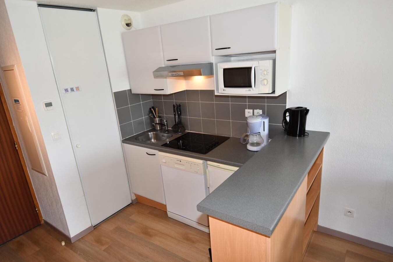 A compact kitchen with white cabinets, a built-in microwave, a coffee maker, and a dishwasher.