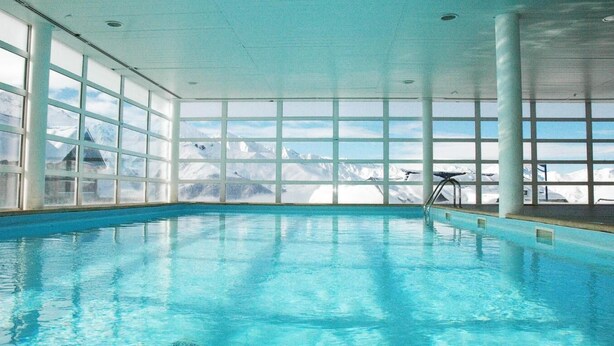 An indoor swimming pool with large windows offering a view of snow-capped mountains.