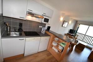 A modern kitchen with a built-in microwave, stove, and dishwasher. There is a wooden dining area with a table and chairs, and a balcony with a railing. - Wifi, fitness, swimming pool, sauna, terrace, balcony, ski locker, 36-42m², Peyragudes (Germ)