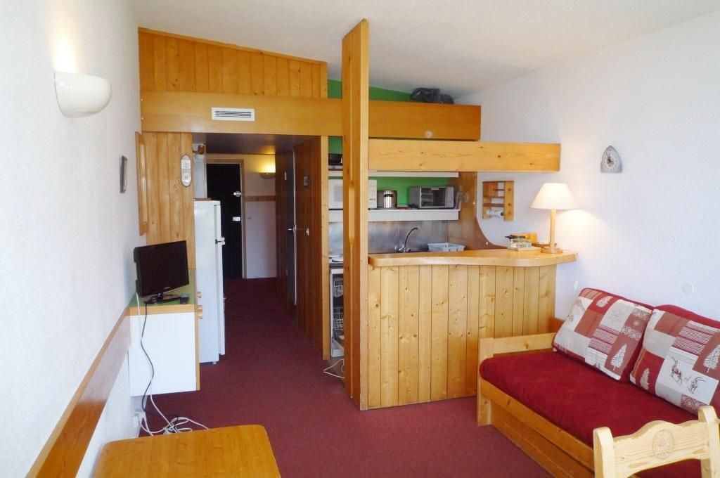 A compact room with a kitchenette, a wooden bed, and a television.