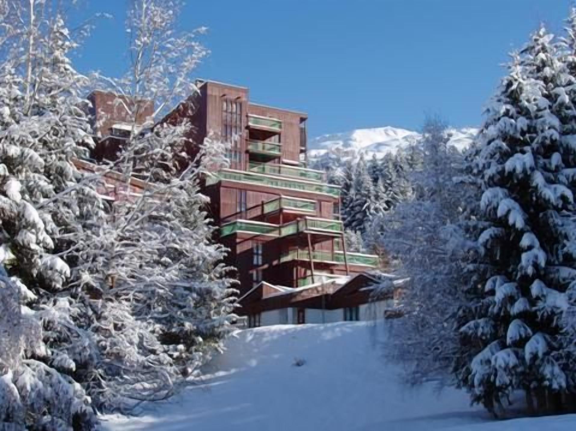 Un immeuble à plusieurs étages doté de balcons, entouré d’arbres couverts de neige.