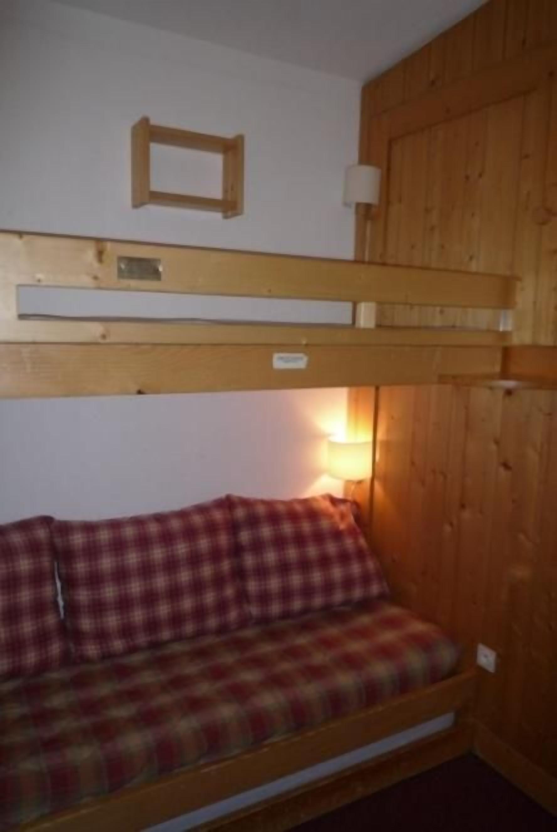A bunk bed with a checkered blanket and a wooden headboard.